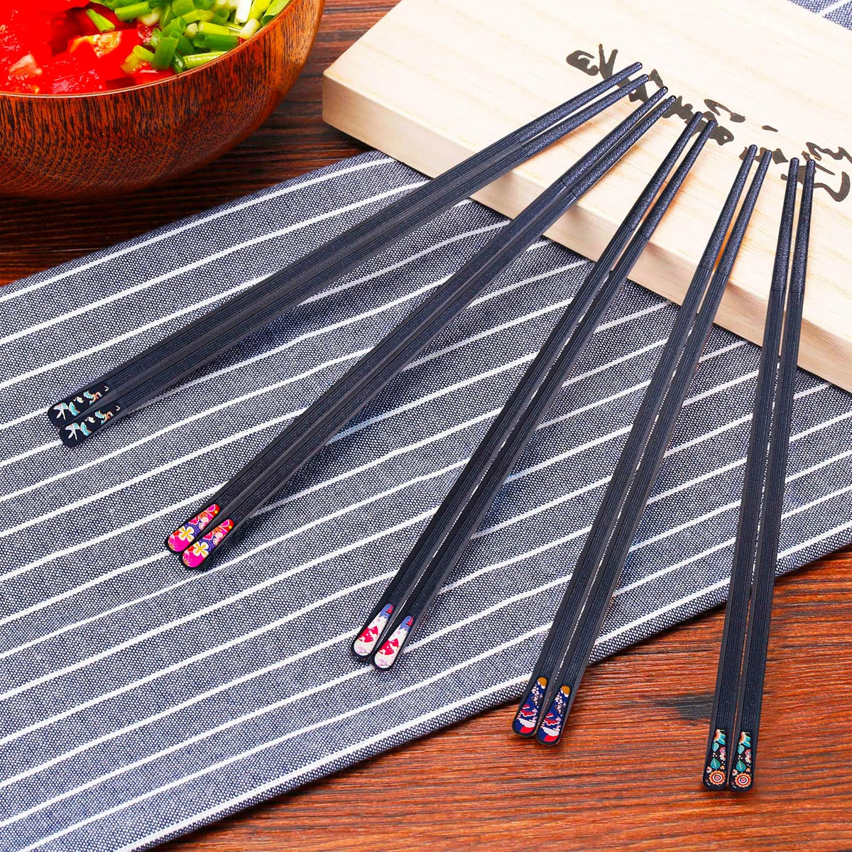 Set of black chopsticks with colorful ends on a striped placemat.