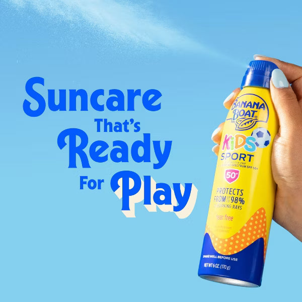 A hand holding a can of Banana Boat Kids Sport sunscreen spray against a bright blue sky background with the text 'Suncare That's Ready For Play'.